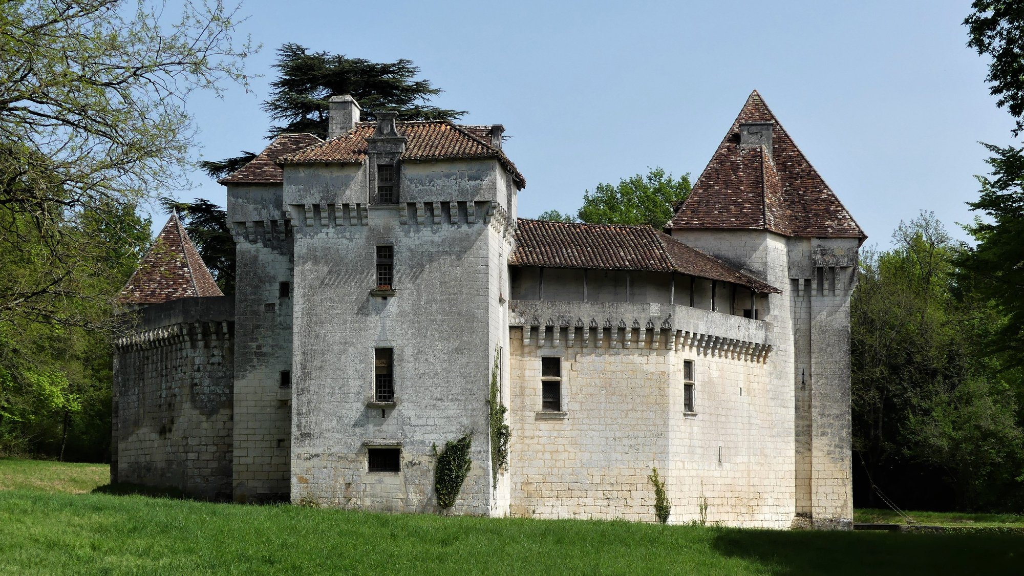 Le château de Caussade vu depuis la prairie : la tour portière carrée, la courtine et la tour d'angle coiffée en poivrière